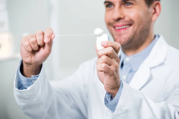Enfoque selectivo del hilo dental en manos del dentista sonriente - foto de stock