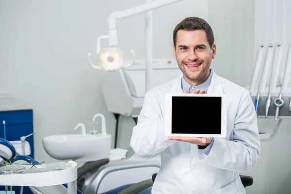 Веселий стоматолог у білому пальто тримає цифровий планшет з порожнім екраном — стокове фото
