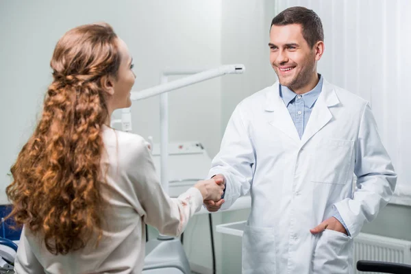 Mujer estrechando las manos con dentista de pie con la mano en el bolsillo - foto de stock