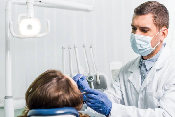 Zahnarzt in Latexhandschuhen und Maske arbeitet mit Frau in Klinik — Stockfoto