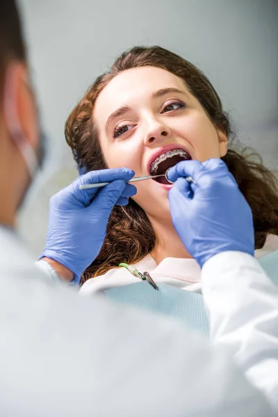 Focalizzazione selettiva di donna attraente in bretelle durante esame di denti vicino a dentista — Foto stock