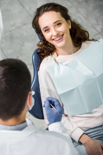 Selective focus of happy woman in braces during examination of teeth near dentist — Stock Photo