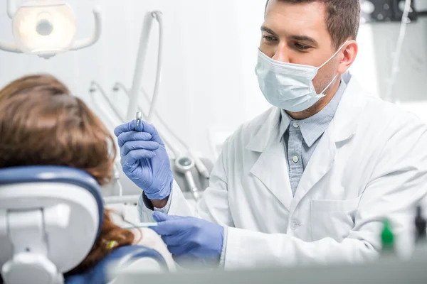 Enfoque selectivo del dentista en máscara examinando paciente femenina - foto de stock