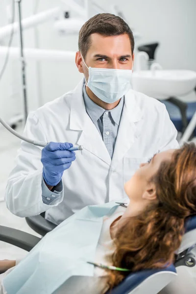 Selektiver Fokus des Zahnarztes in weißem Kittel und Maske, der Patientin untersucht — Stockfoto