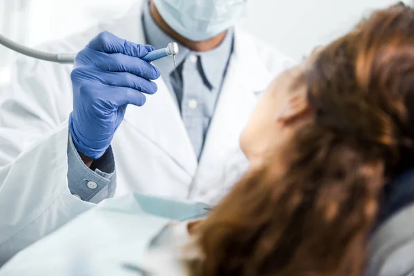 Visão recortada do dentista em jaleco branco segurando instrumento dentário perto de paciente do sexo feminino — Fotografia de Stock