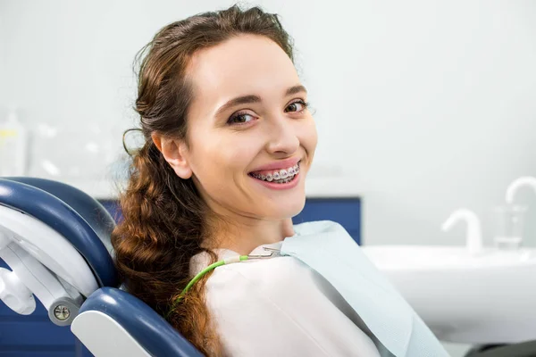 Mujer feliz en frenos sonriendo durante el examen en la clínica dental - foto de stock