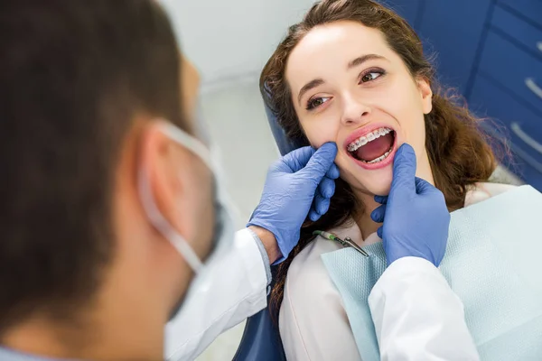 Foco seletivo da mulher em aparelho de abrir a boca durante o exame dos dentes perto do dentista — Fotografia de Stock