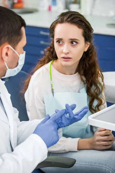 Enfoque selectivo de la mujer molesta mirando al dentista en guantes de látex y máscara - foto de stock
