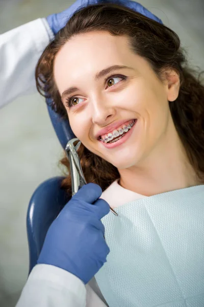 Selective focus of woman in braces smiling while looking at dentist during examination — Stock Photo