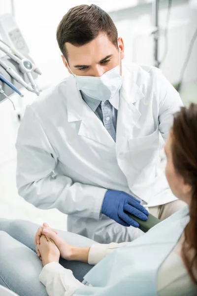 Messa a fuoco selettiva del dentista in maschera guardando la donna in clinica dentale — Foto stock