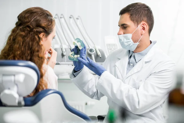 Foco seletivo do dentista em luvas de látex mostrando modelo de dentes perto de paciente do sexo feminino — Fotografia de Stock