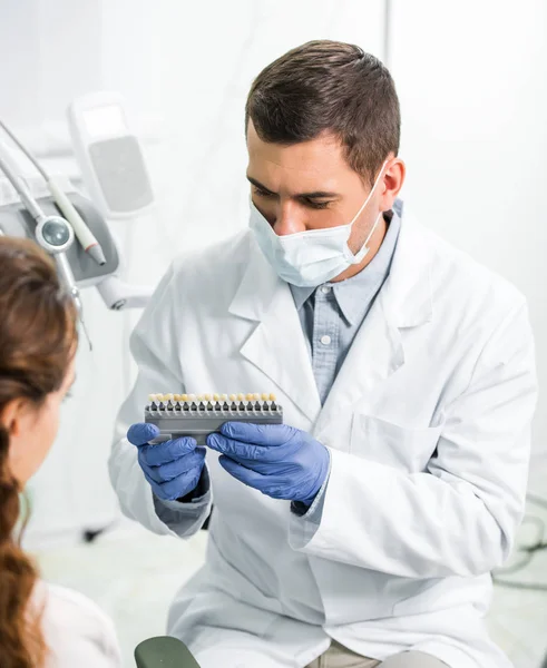 Woman selecting teeth color palette near dentist in mask and latex gloves — Stock Photo