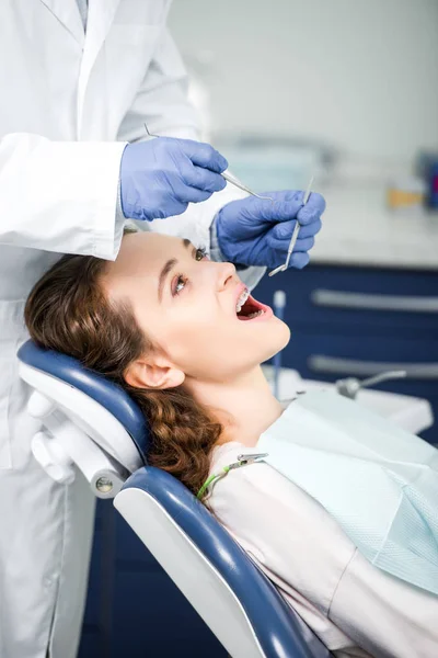 Visão recortada do dentista em luvas de látex examinando a mulher em aparelho com boca aberta — Fotografia de Stock
