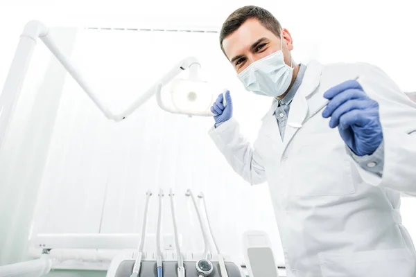 Dentista em luvas de látex e máscara segurando instrumento dentário e lâmpada dental — Fotografia de Stock