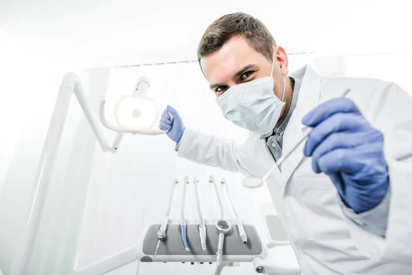 Dentista in guanti di lattice e maschera con lampada dentale e strumento dentale in mano — Foto stock