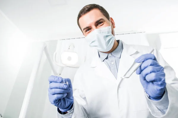 Dentiste en gants de latex et masque tenant les instruments dentaires dans les mains — Photo de stock