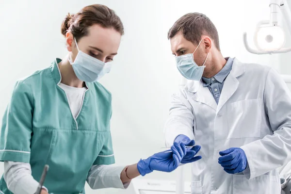 Dentista masculino dando instrumento odontológico a colega de máscara — Fotografia de Stock