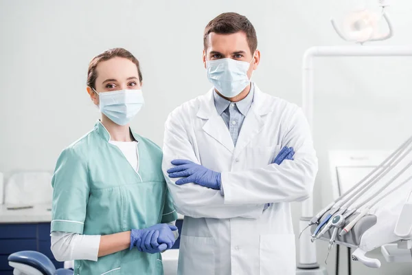 Female dentist in mask standing near coworker with crossed arms in dental clinic — Stock Photo