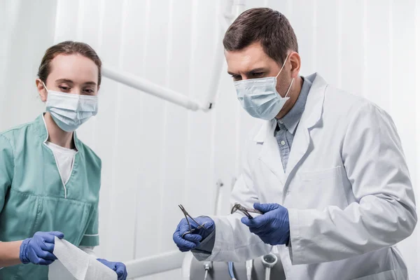 Female dentist standing near colleague in mask with dental instruments — Stock Photo