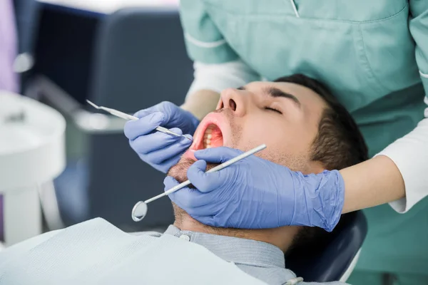 Обрезанный вид женщины-стоматолога в латексных перчатках, осматривающей пациента с открытым ртом — стоковое фото