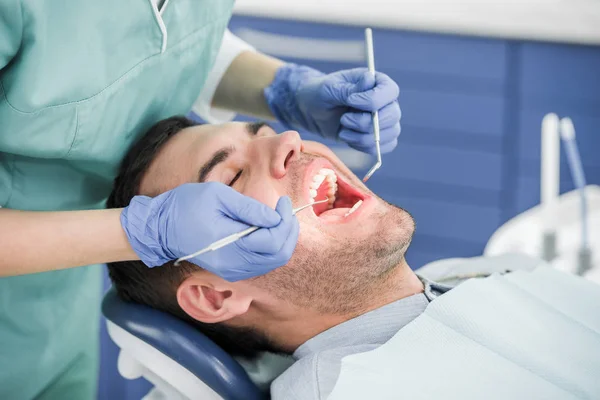 Vista ritagliata del dentista in guanti di lattice esaminando il paziente con bocca aperta — Stock Photo