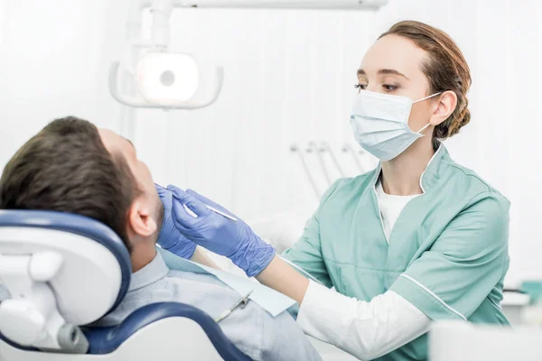 Dentista femenina sosteniendo instrumentos dentales cerca del paciente en la clínica dental - foto de stock