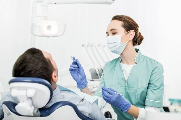 Dentista feminina em máscara segurando instrumentos dentários perto do paciente na clínica odontológica — Fotografia de Stock