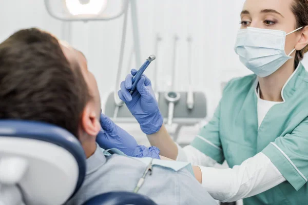 Zahnärztin in Maske hält zahnärztliches Instrument, während sie Gesicht der Patientin in Zahnklinik berührt — Stockfoto