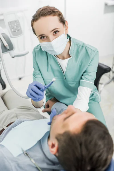 Zahnärztin in Maske hält Zahnbohrer während der Arbeit mit Patientin in Zahnklinik — Stockfoto
