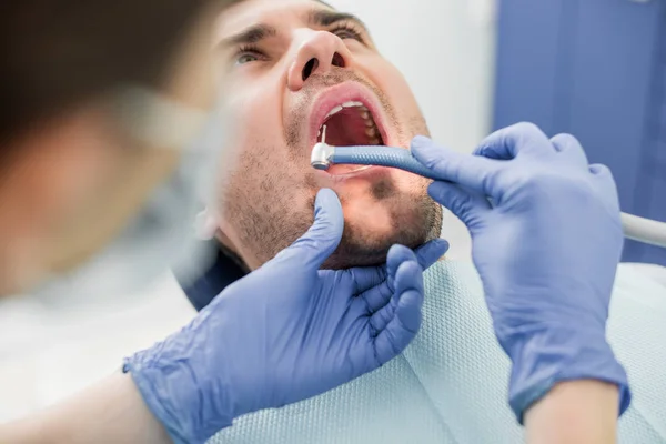Dentista en la máscara de perforación de dientes mientras trabaja con el paciente en la clínica dental - foto de stock