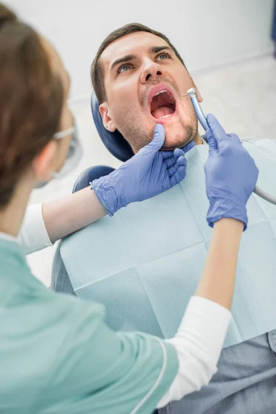 Patient avec bouche ouverte près du dentiste tenant une perceuse dentaire — Photo de stock
