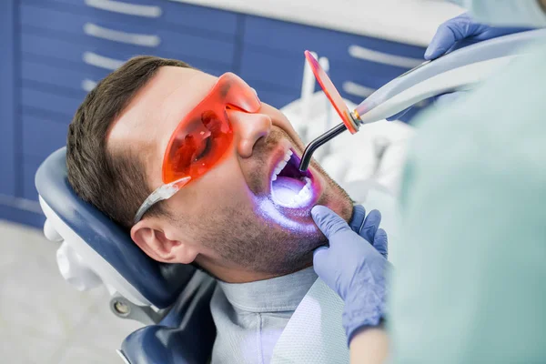 Vista recortada del dentista haciendo procedimiento de blanqueamiento para el paciente en gafas - foto de stock