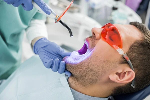 Vue recadrée du dentiste faisant la procédure de blanchiment au patient dans des lunettes — Photo de stock