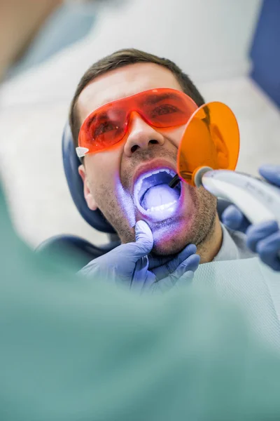 Enfoque selectivo del paciente con la boca abierta durante el procedimiento de blanqueamiento cerca del dentista - foto de stock