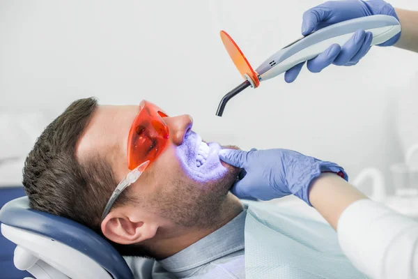 Vue recadrée du dentiste faisant la procédure de blanchiment au patient — Photo de stock