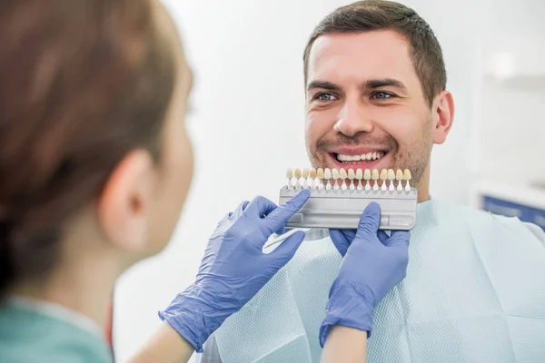 Selective focus of man smiling near dentist with teeth color palette in hands — Stock Photo