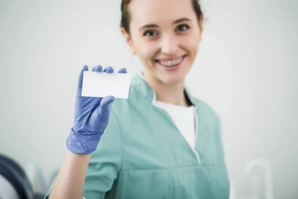 Selective focus of blank card in hand of cheerful female dentist — Stock Photo