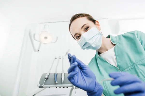 Selective focus of female dentist in mask and latex gloves holding dental instrument — Stock Photo