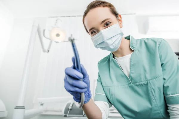 Enfoque selectivo del dentista en la máscara y guantes de látex que sostienen taladro dental - foto de stock