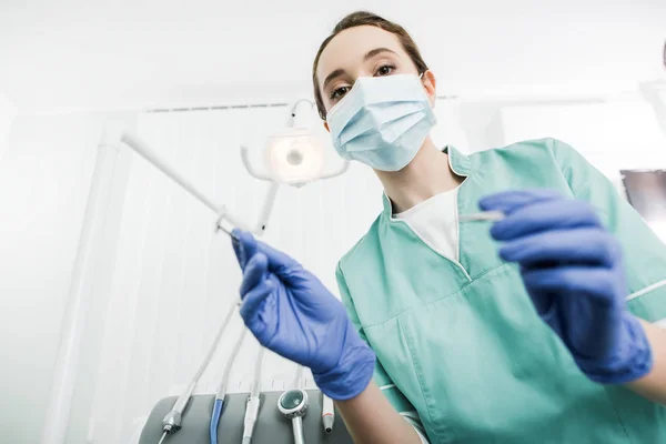 Enfoque selectivo del dentista en la máscara y guantes de látex que sostienen instrumentos dentales - foto de stock