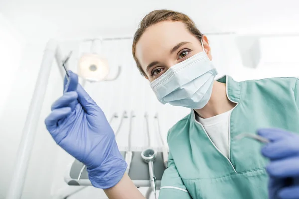 Селективное внимание женщины-стоматолога в латексных перчатках и маске, держащей стоматологические инструменты — стоковое фото