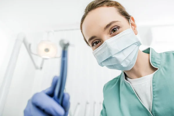 Селективное внимание женщины-стоматолога в латексных перчатках и маске, держащей зубную дрель — стоковое фото