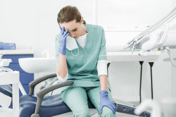 Виснажений стоматолог тримає голову, сидячи на стільці в стоматологічній клініці — стокове фото