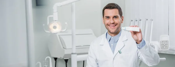 Красивый стоматолог с зубной пастой, улыбающийся в стоматологической клинике — стоковое фото
