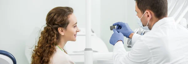 Dentista em luvas de látex apontando com o dedo na radiografia dos dentes perto do paciente — Fotografia de Stock