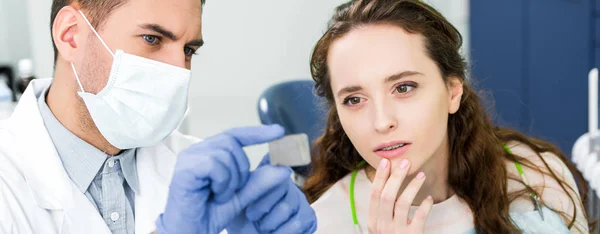 Enfoque selectivo de la mujer reflexiva mirando la radiografía de los dientes en manos del dentista en guantes de látex y máscara - foto de stock