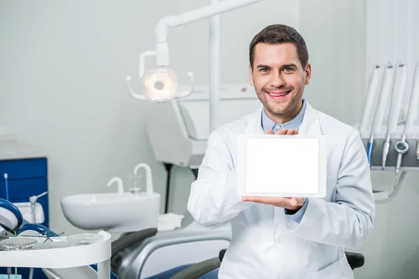 Alegre dentista sosteniendo tableta digital con pantalla en blanco en clínica dental - foto de stock