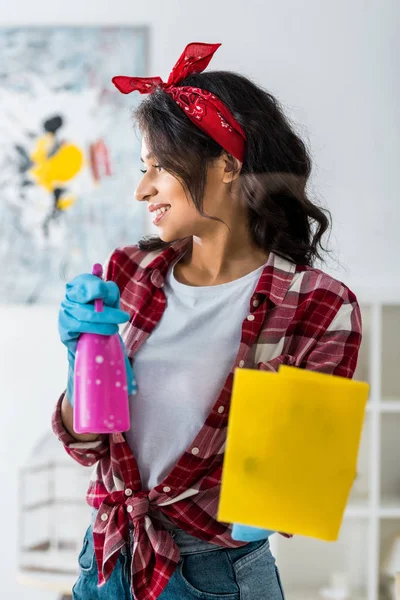 Pretty african american woman holding pink spray bottle and yellow rag — Stock Photo