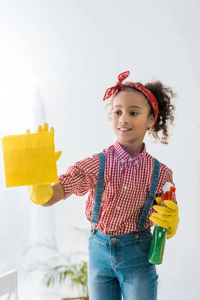 Cute african american child with yellow rag and green spray bottle — Stock Photo