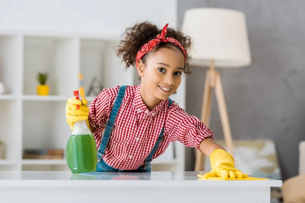 Cute african american child cleaning table with yellow rag — Stock Photo